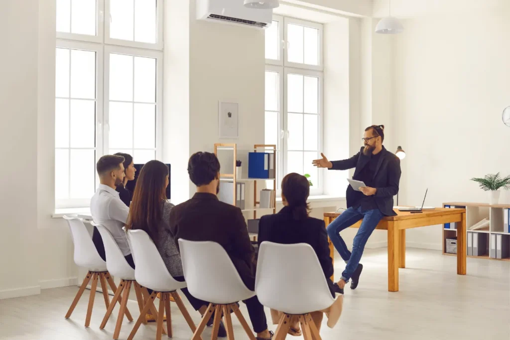 Coach leading a seated sales team session in a bright room